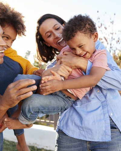 Young mixed race parents playing outdoors carrying their children in the garden Young mixed race parents playing outdoors carrying their children in the garden